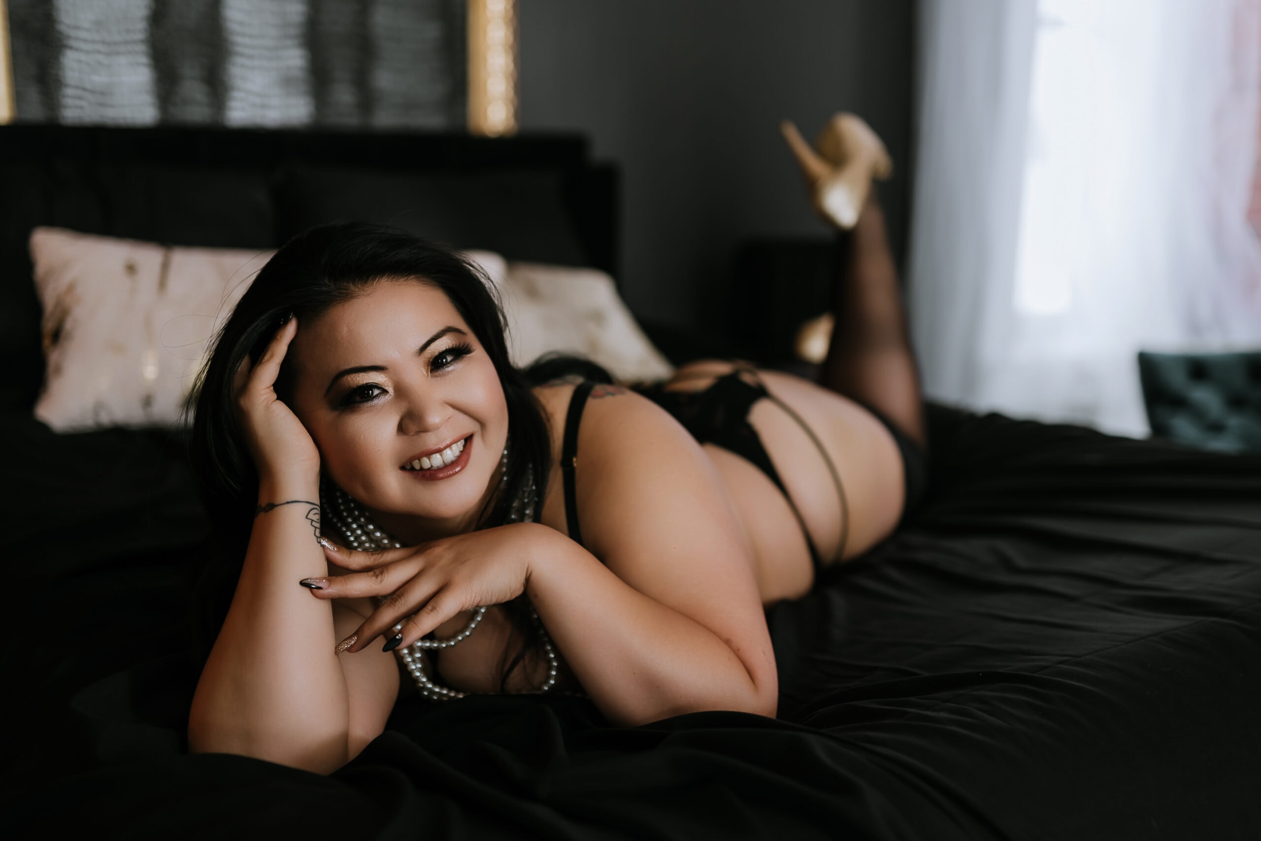 Plus sized woman on bed smiling at camera. Photo by Katie O'Docharty, Denver Boudoir Photographer.
